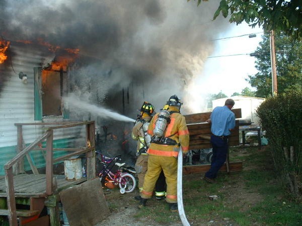 The Engine crew making the initial hit on a mobile home fire on Grant Street as Past Chief Allen Fowler moves a picnic table out of the way.